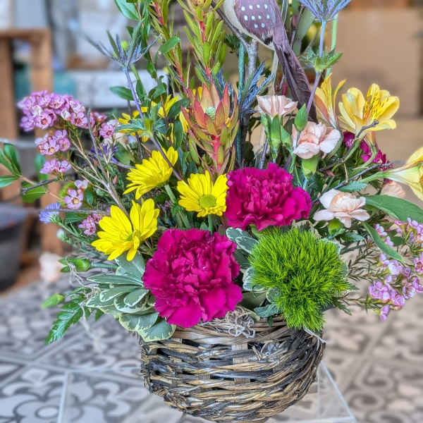 Mixed flower arrangement in a woven basket with a decorative bird