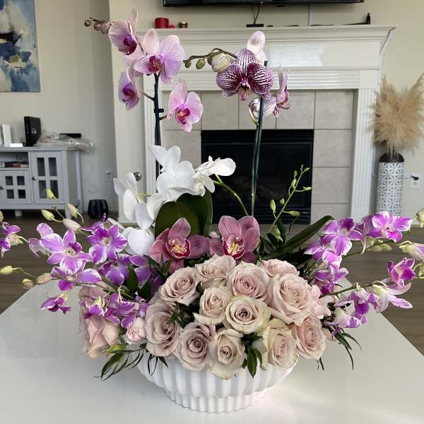 Pink and purple orchids with pale roses in a white vase