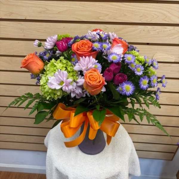 Bouquet of orange roses and purple daisies in a vase with an orange ribbon