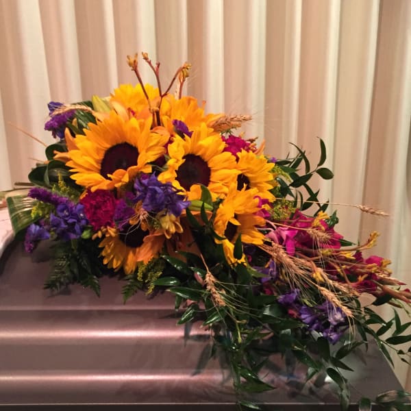 Sunflower arrangement with purple and pink flowers on a casket
