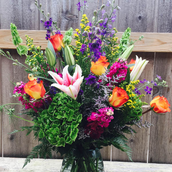 Colorful mixed bouquet in a glass vase with roses, lilies, and purple flowers