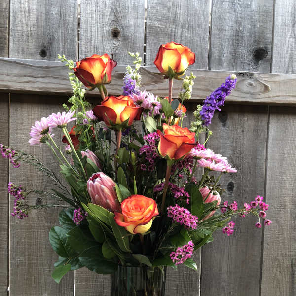 Tall bouquet of orange-red roses and pink flowers in a glass vase