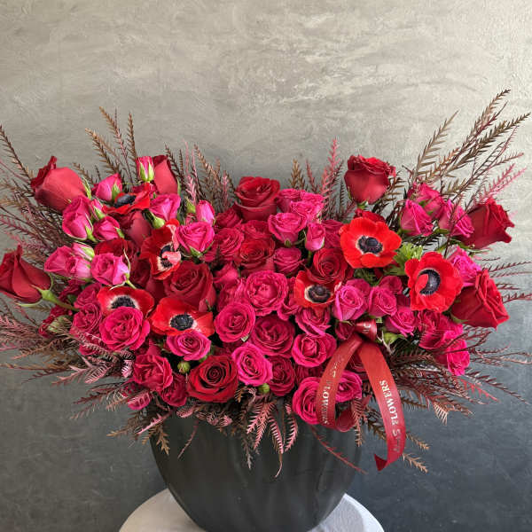 Red and hot pink roses arranged in a black vase with red ribbon