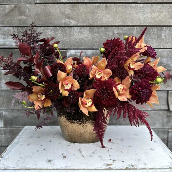 Deep burgundy and peach flowers arranged in a gold vase
