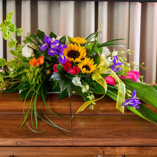 Colorful floral casket spray with sunflowers, roses, and orchids