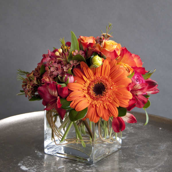 Orange gerbera daisies and red roses in a clear square vase