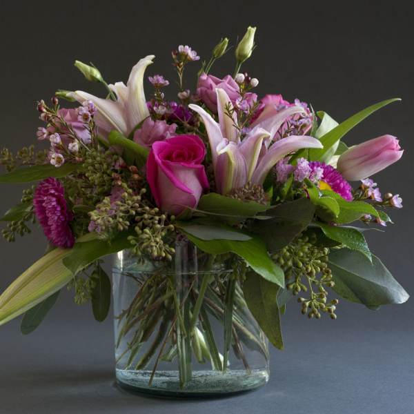 Pink lilies and roses arranged in a clear glass vase