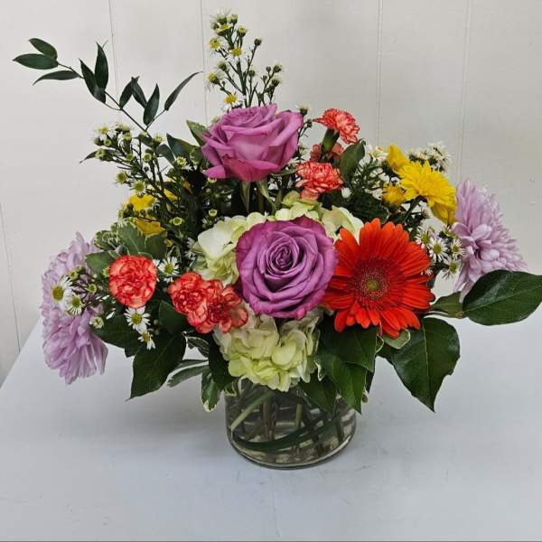 Mixed bouquet with purple roses, gerbera daisy, carnations, and hydrangea in a glass vase
