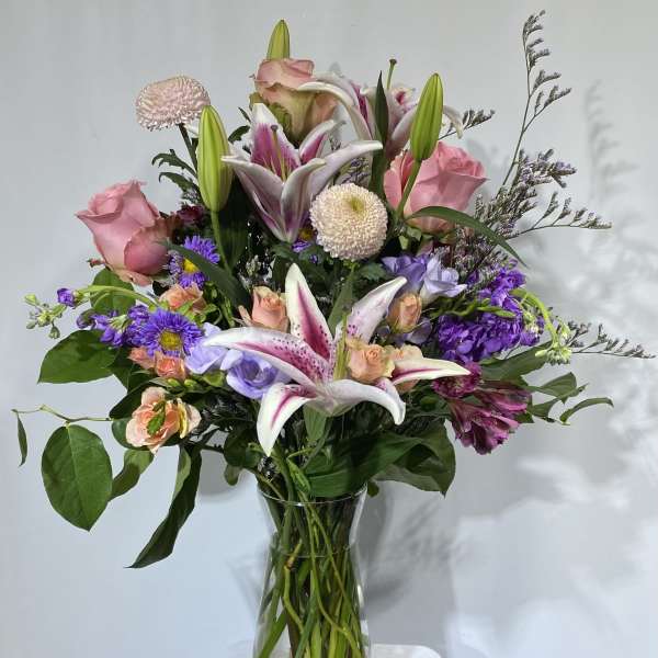 Mixed bouquet of pink roses, lilies, and purple flowers in a glass vase
