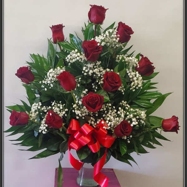 Red roses arranged in a clear vase with baby's breath and a red ribbon