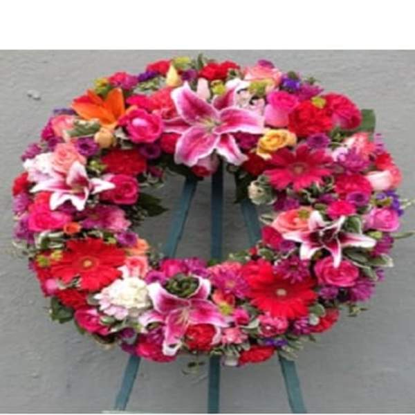 Circular floral wreath with pink, red, and white blooms on a stand