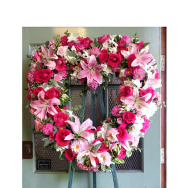 Heart-shaped floral wreath with pink lilies and roses on an easel