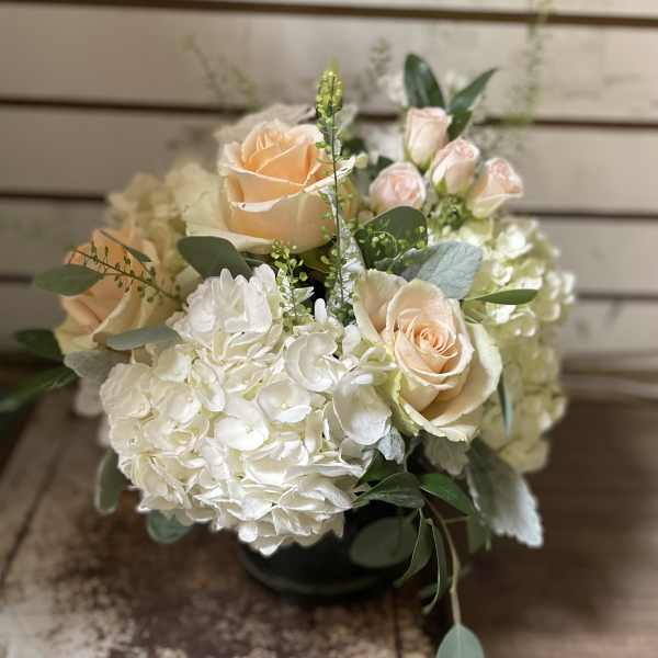 Low round arrangement of peach roses and white hydrangeas in a glass vase