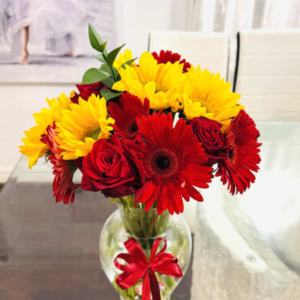 Red and yellow flowers in a clear glass vase with a red ribbon