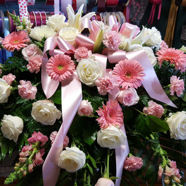 Pink and white floral casket spray with ribbon accents