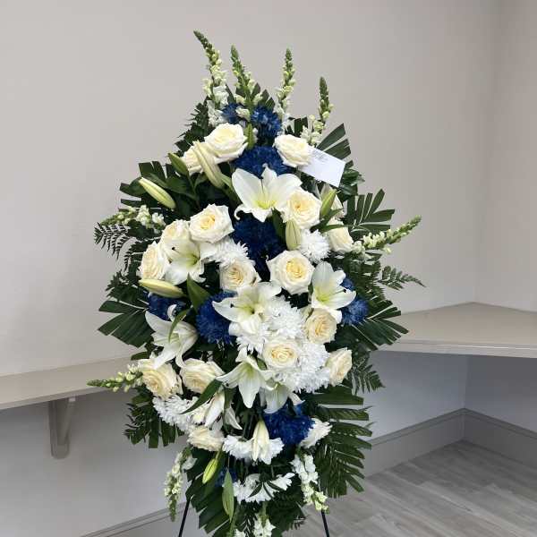 Standing floral spray with white roses, lilies, and blue chrysanthemums on an easel