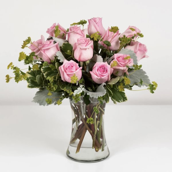 Pink roses arranged in a clear glass vase with mixed greenery