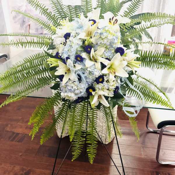 Tall floral spray with white lilies, blue hydrangeas, and fern fronds
