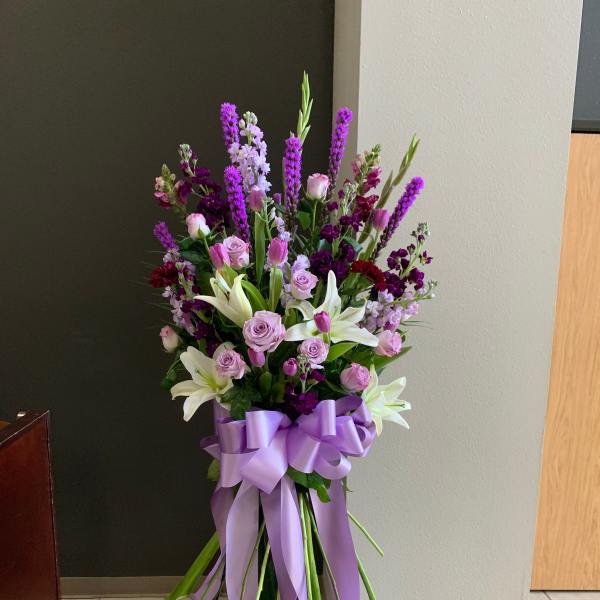 Tall bouquet of pink and purple flowers with white lilies and a lavender ribbon