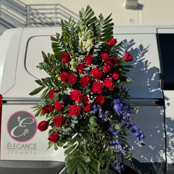 Tall standing spray of red roses and blue flowers with greenery