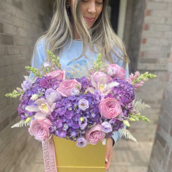 Large pink and purple flower arrangement in a gold box