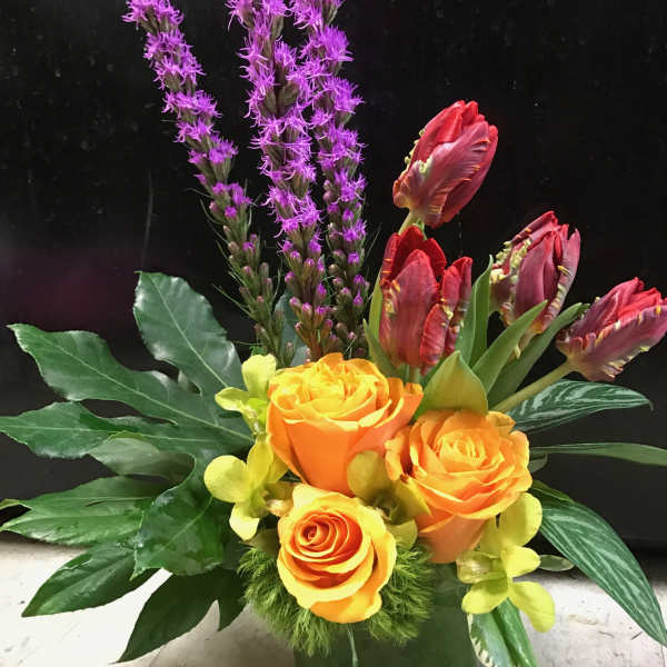 Orange roses with purple spikes and red tulips in a green vase