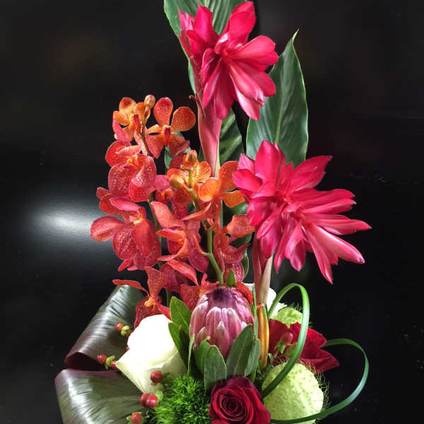 Tropical floral arrangement with pink orchids and red roses in a wrapped container