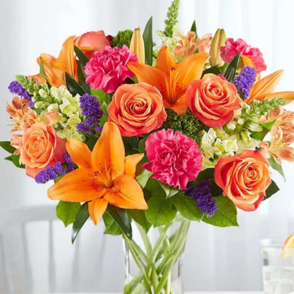 Bouquet of orange lilies, coral roses, and pink carnations in a glass vase