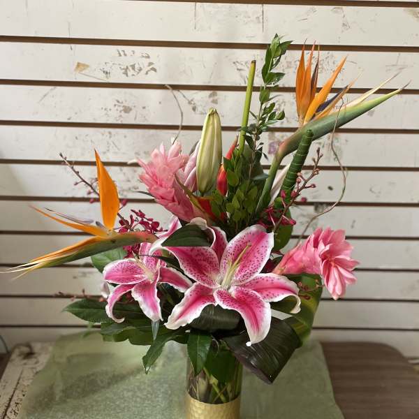 Tall tropical arrangement with pink lilies and orange bird of paradise in a gold vase