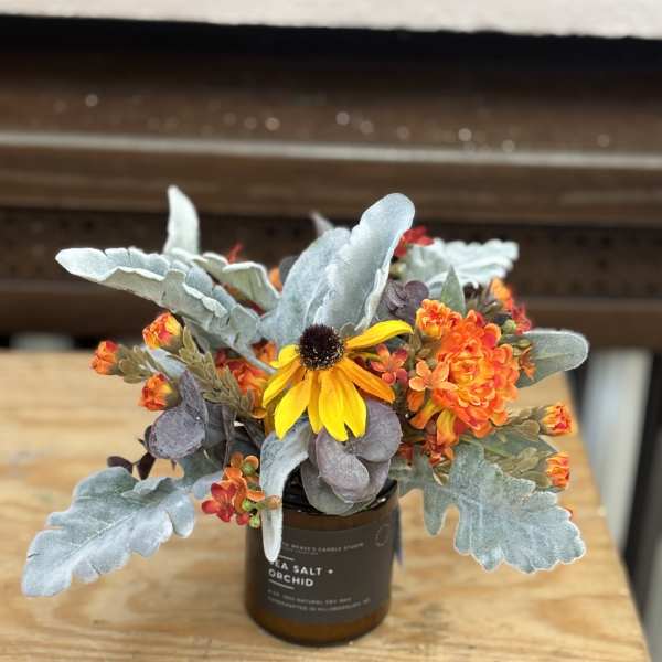 Small floral arrangement in a brown candle jar with yellow and orange blooms