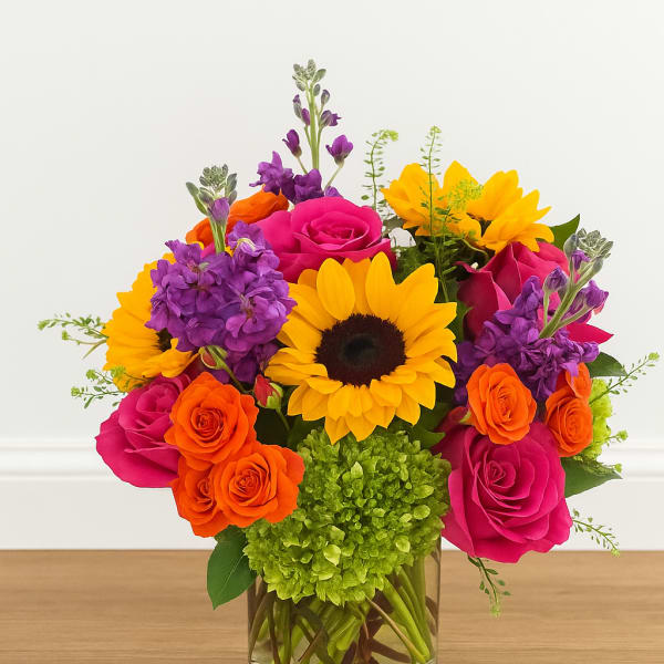 Bright bouquet of sunflowers, pink roses, and purple flowers in a glass vase