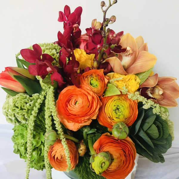 Bright bouquet of orange ranunculus and orchids in a vase