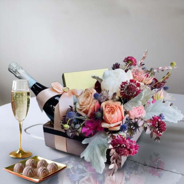 Flower arrangement in a gift box with a champagne bottle, flute, and chocolates