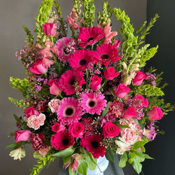 Large pink and green floral arrangement in a white vase