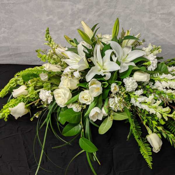 White floral casket spray with lilies, roses, and trailing greenery