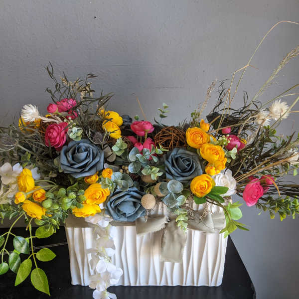 Colorful floral arrangement in a white pleated container with blue and yellow blooms