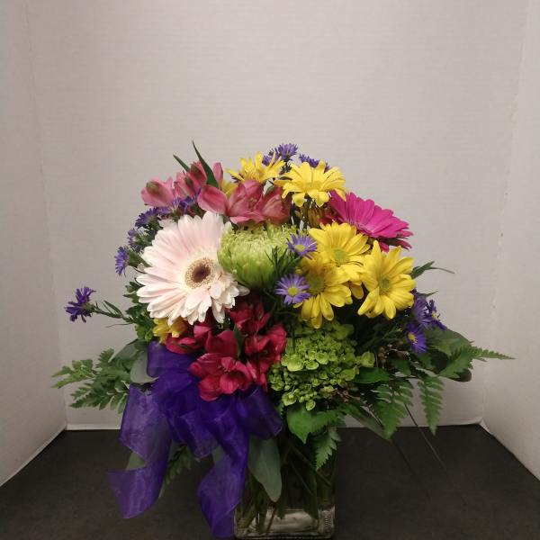 Mixed bouquet of daisies and alstroemeria in a glass vase with a purple ribbon