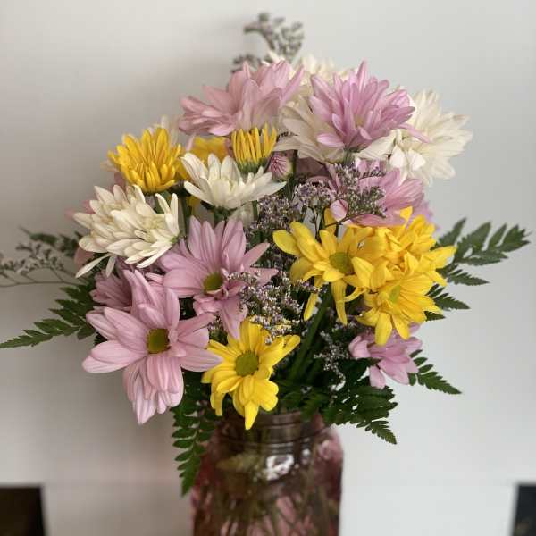 Pink, white, and yellow daisy bouquet in a pink glass vase