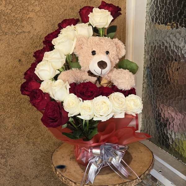 Red and white roses arranged with a teddy bear and ribbon