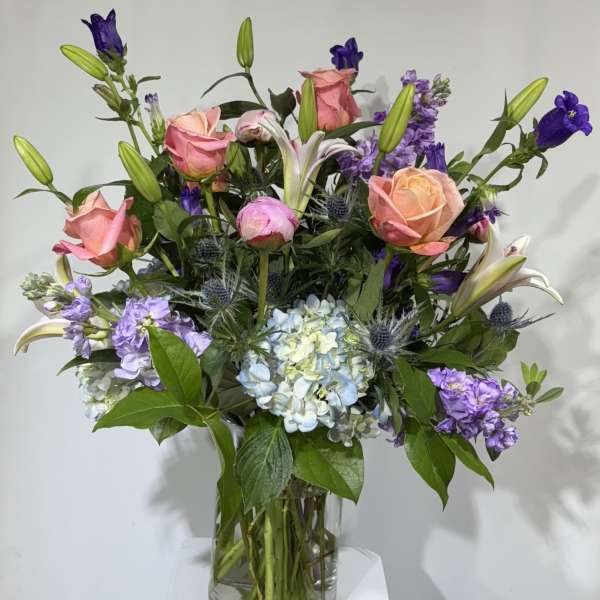 Mixed bouquet of pink roses, lilies, and purple flowers in a glass vase