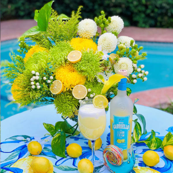 Yellow and white floral arrangement with lemons and a bottle on a table