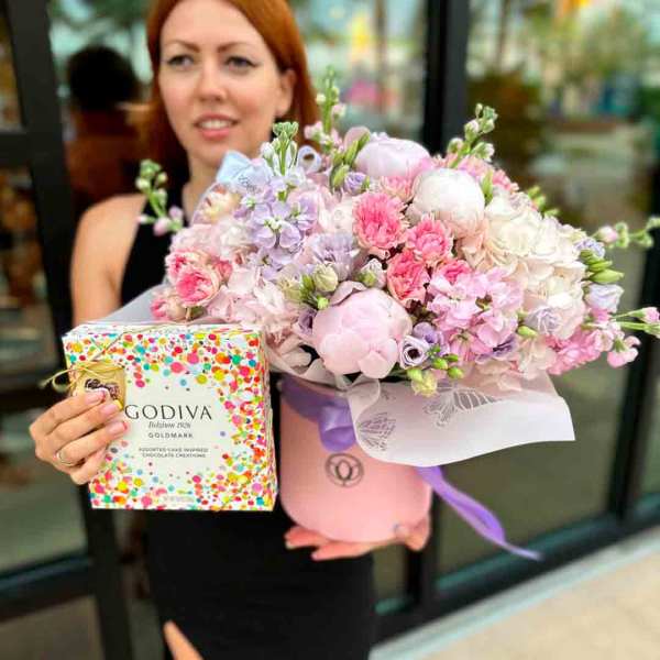 Pink and lavender flower arrangement in a round box with a chocolate gift box