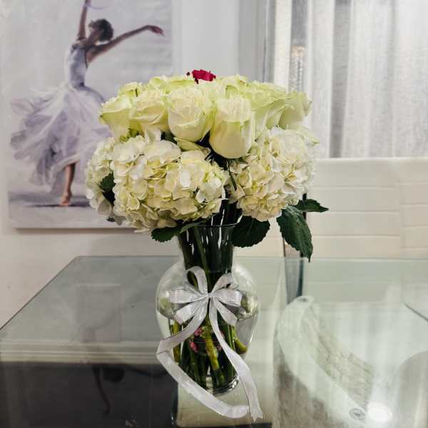 White roses and hydrangeas in a clear vase with a silver ribbon