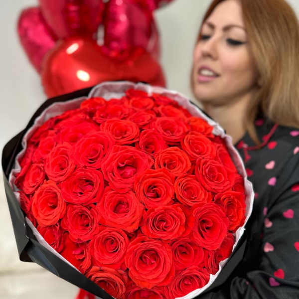 Large bouquet of red roses held in front of a woman with red balloons behind her