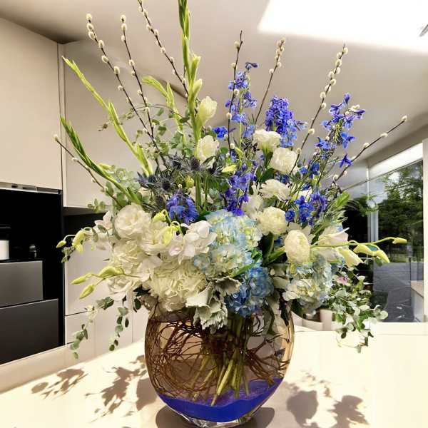 Tall blue and white floral arrangement in a glass vase