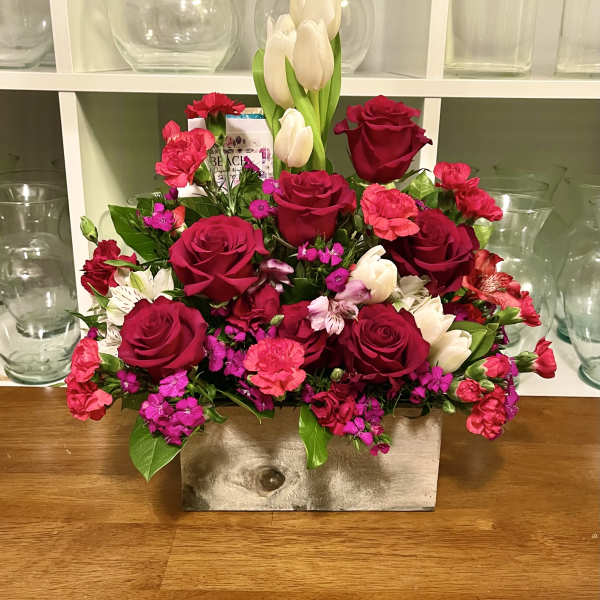 Mixed bouquet of red roses, pink carnations, and white tulips in a rectangular vase