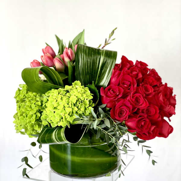 Red roses and pink tulips with green hydrangeas in a glass vase