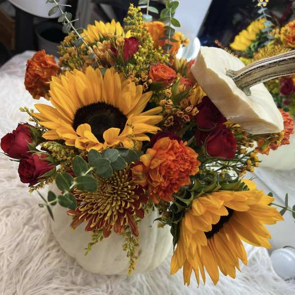 Autumn bouquet with sunflowers, red roses, and orange blooms in a white pumpkin vase.