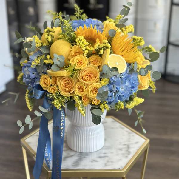 Yellow roses and blue hydrangeas in a white vase with lemon slices