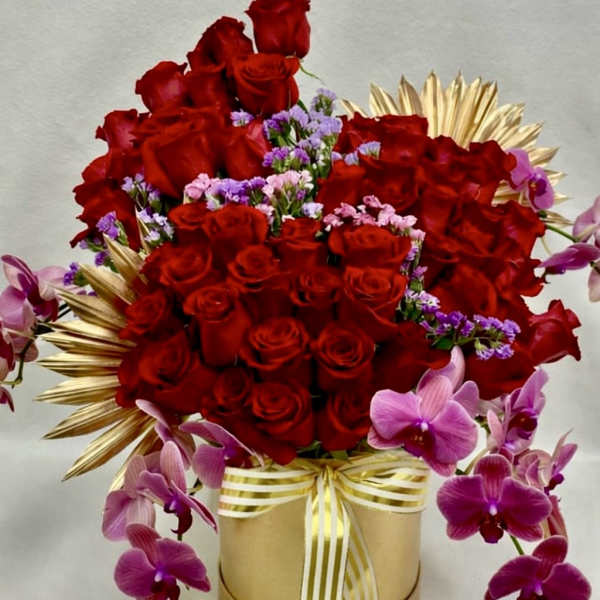 Red roses and purple orchids arranged in a gold box with ribbon
